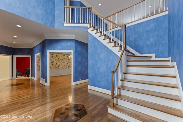 stairway featuring wood finished floors, baseboards, recessed lighting, a towering ceiling, and crown molding