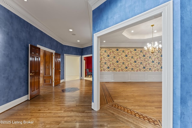 hallway featuring wood finished floors, recessed lighting, wainscoting, crown molding, and a notable chandelier