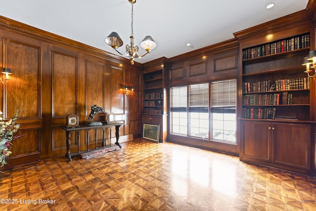 office space with built in features, a notable chandelier, wood walls, and a decorative wall