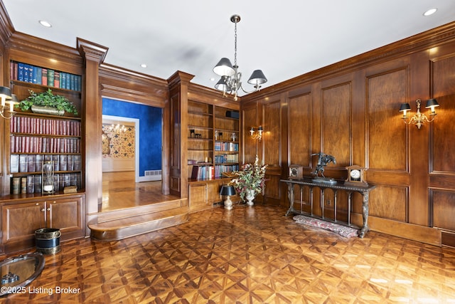 office space with visible vents, crown molding, built in features, a notable chandelier, and a decorative wall