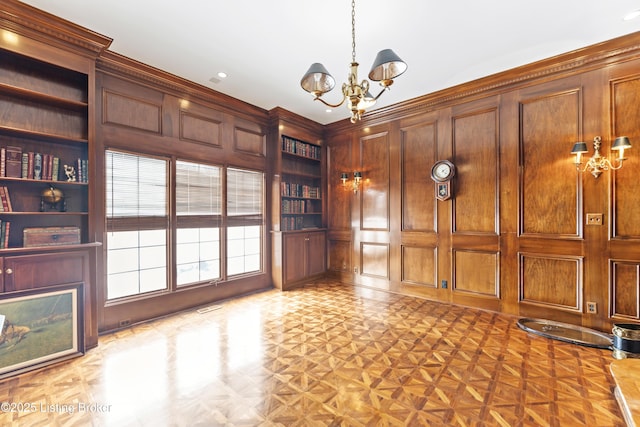 unfurnished living room featuring a notable chandelier, built in shelves, a decorative wall, and wooden walls