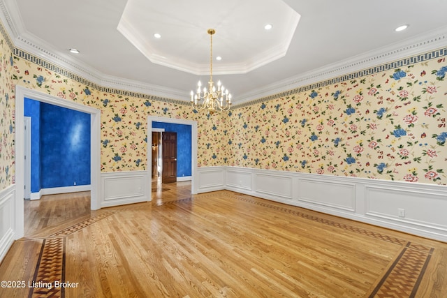 unfurnished room featuring a wainscoted wall, light wood finished floors, an inviting chandelier, a tray ceiling, and crown molding