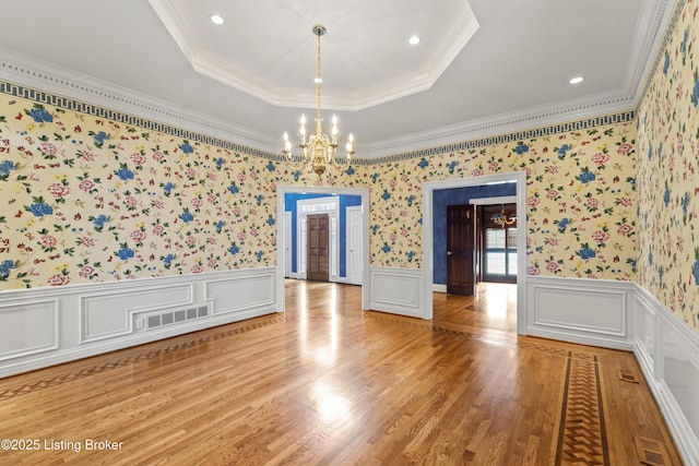 unfurnished room with a wainscoted wall, visible vents, a tray ceiling, light wood-style flooring, and a notable chandelier