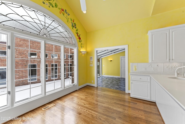 unfurnished dining area with baseboards, visible vents, light wood finished floors, a sink, and vaulted ceiling