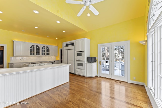 kitchen with glass insert cabinets, light countertops, lofted ceiling, light wood-style floors, and white appliances