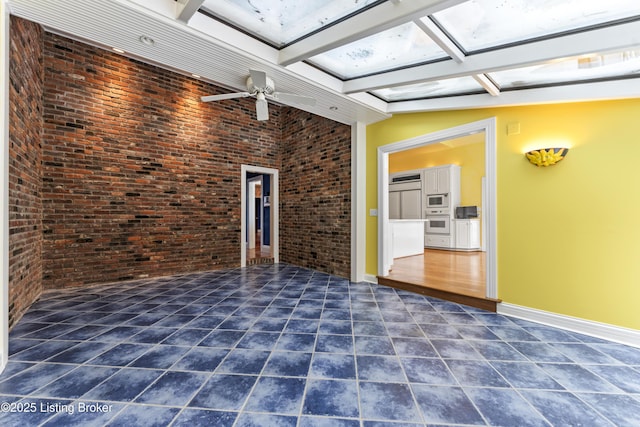 spare room featuring dark tile patterned floors, brick wall, a skylight, and baseboards