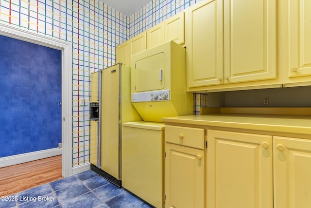 interior space with laundry area, wallpapered walls, stacked washing maching and dryer, and baseboards