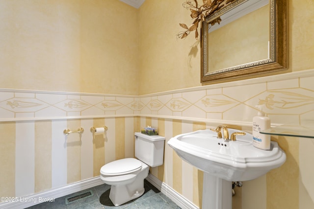 half bathroom with tile patterned floors, visible vents, wainscoting, and toilet