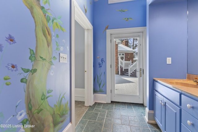 doorway to outside with stone finish flooring, baseboards, and a sink