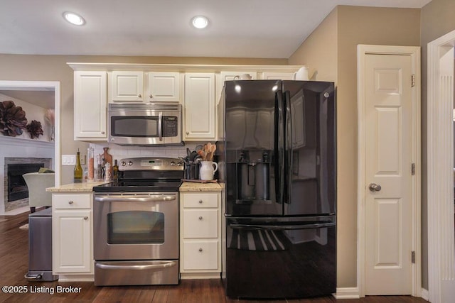 kitchen with tasteful backsplash, dark wood finished floors, a fireplace with flush hearth, stainless steel appliances, and white cabinetry