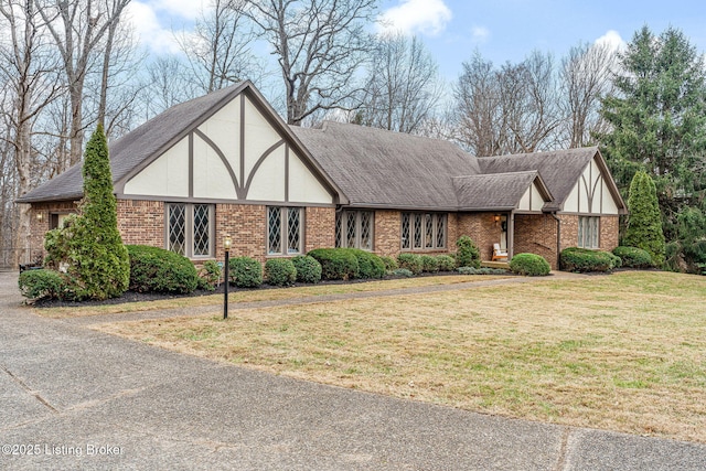 tudor-style house with stucco siding, a shingled roof, a front yard, and brick siding