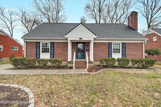 view of front of property featuring brick siding, a chimney, a front lawn, and roof with shingles