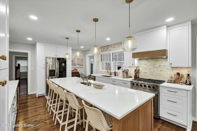 kitchen with appliances with stainless steel finishes, dark wood-style flooring, light countertops, premium range hood, and a sink