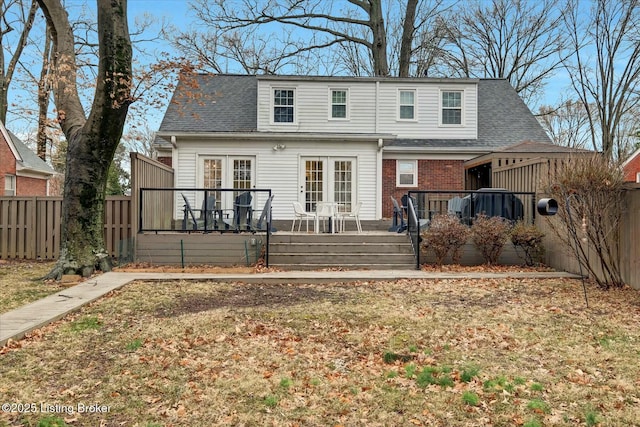 rear view of house featuring a deck, brick siding, roof with shingles, and a fenced backyard