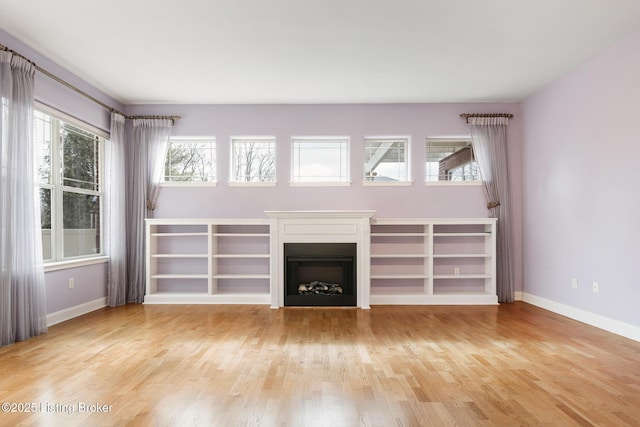 unfurnished living room featuring a wealth of natural light, baseboards, a fireplace, and light wood finished floors