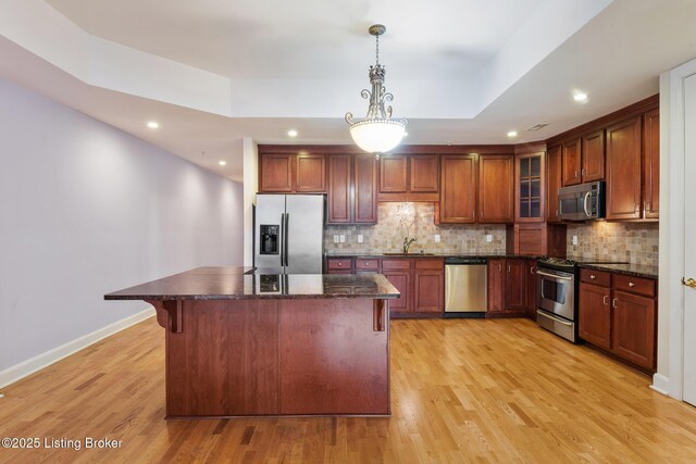 kitchen featuring a tray ceiling, appliances with stainless steel finishes, a sink, and tasteful backsplash