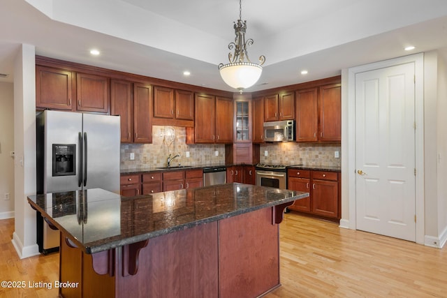 kitchen with a breakfast bar area, a sink, appliances with stainless steel finishes, light wood-type flooring, and tasteful backsplash