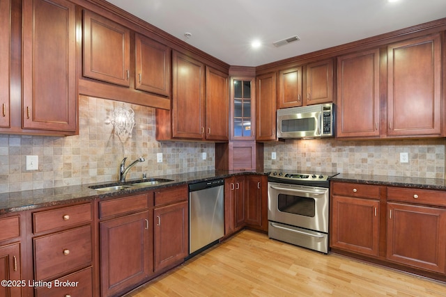 kitchen with light wood finished floors, visible vents, appliances with stainless steel finishes, dark stone countertops, and a sink