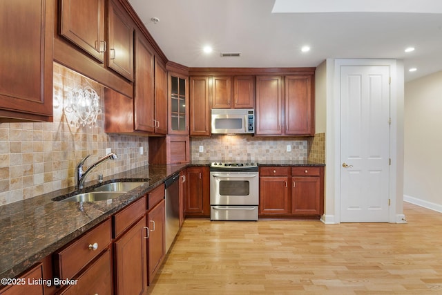 kitchen featuring appliances with stainless steel finishes, glass insert cabinets, a sink, and light wood finished floors