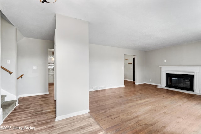 unfurnished living room with baseboards, visible vents, a fireplace with flush hearth, wood finished floors, and stairs