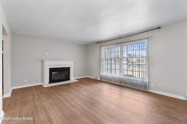 unfurnished living room with a fireplace with flush hearth, a textured ceiling, baseboards, and wood finished floors