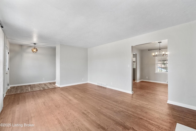 empty room with a chandelier, visible vents, baseboards, and wood finished floors