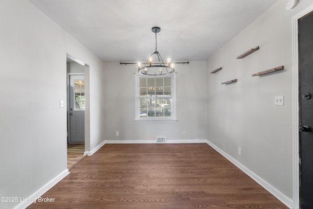 unfurnished dining area with baseboards, visible vents, an inviting chandelier, and wood finished floors