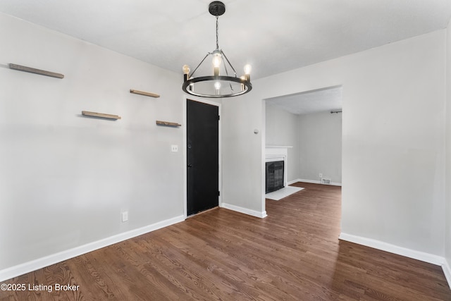 interior space with a fireplace with flush hearth, an inviting chandelier, wood finished floors, and baseboards