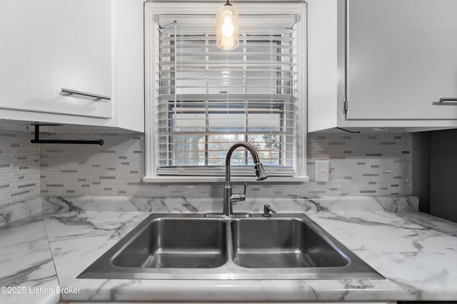 kitchen featuring light stone countertops, tasteful backsplash, white cabinets, and a sink