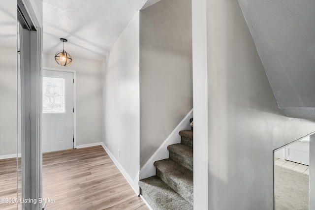 foyer entrance with light wood-style floors, stairs, baseboards, and a textured ceiling