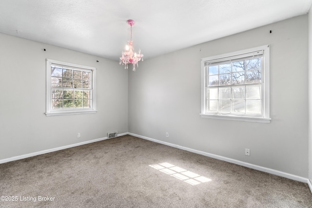 carpeted spare room featuring plenty of natural light, visible vents, and baseboards