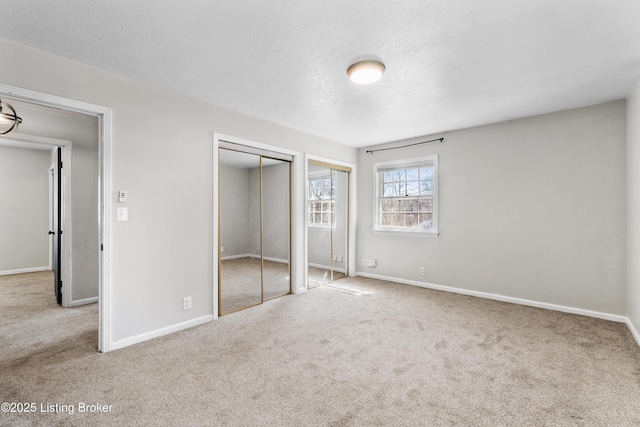 unfurnished bedroom featuring carpet flooring, a textured ceiling, baseboards, and two closets