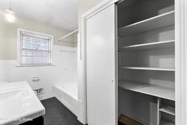 full bathroom featuring a wainscoted wall, visible vents, tile walls, tile patterned floors, and washtub / shower combination