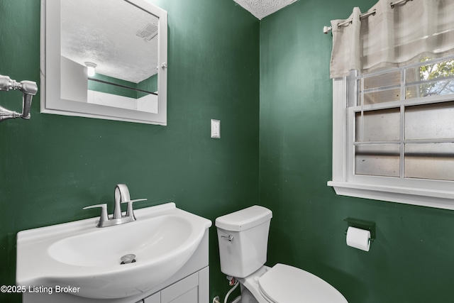 half bath featuring a textured ceiling, vanity, and toilet