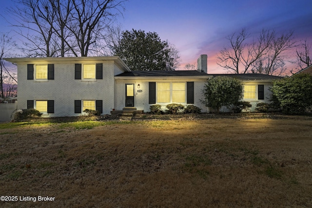 tri-level home with brick siding, a lawn, and a chimney