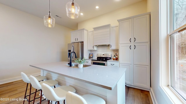 kitchen with a breakfast bar area, light wood-style flooring, backsplash, appliances with stainless steel finishes, and a kitchen island with sink