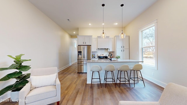 kitchen with a center island with sink, white cabinets, decorative backsplash, appliances with stainless steel finishes, and a breakfast bar area