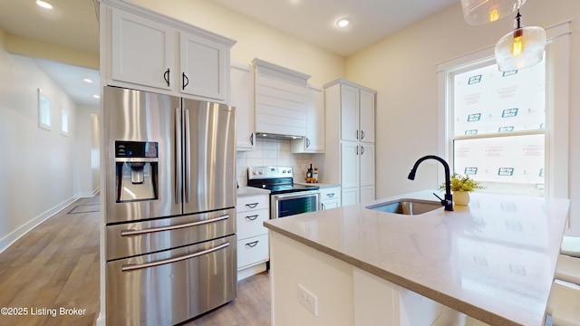 kitchen with light wood finished floors, tasteful backsplash, appliances with stainless steel finishes, a kitchen island with sink, and a sink