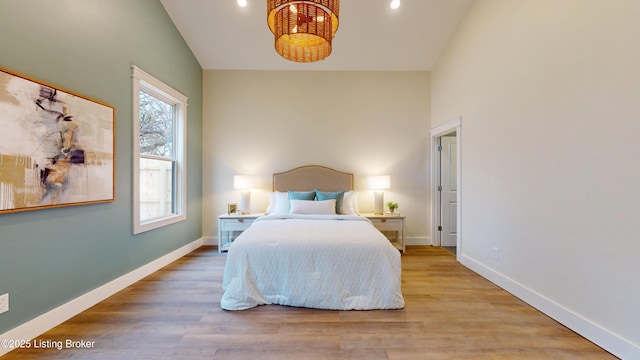 bedroom with high vaulted ceiling, wood finished floors, and baseboards