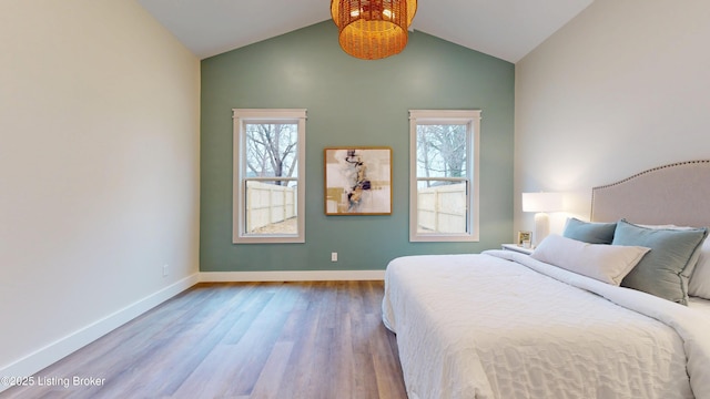 bedroom featuring lofted ceiling, multiple windows, baseboards, and wood finished floors