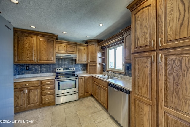 kitchen featuring under cabinet range hood, stainless steel appliances, a sink, light countertops, and decorative backsplash