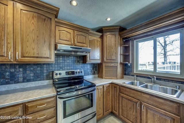 kitchen with under cabinet range hood, brown cabinetry, a sink, and stainless steel range with electric cooktop