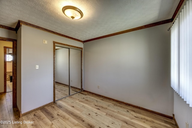 unfurnished bedroom with a textured ceiling, crown molding, a closet, and light wood-style floors