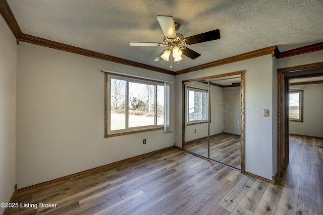 unfurnished bedroom featuring multiple windows, crown molding, light wood-style flooring, and a textured ceiling