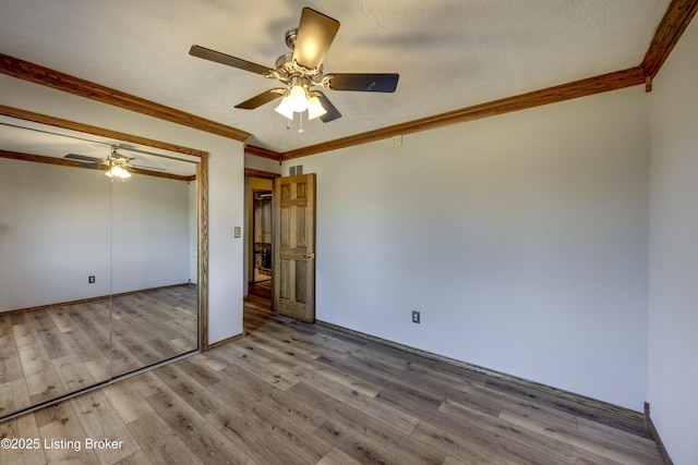 unfurnished bedroom with crown molding, a closet, a ceiling fan, a textured ceiling, and light wood-type flooring