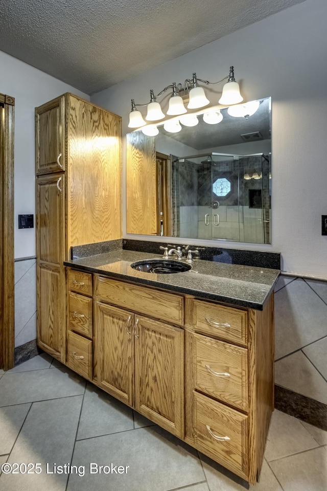 bathroom with a textured ceiling, tile patterned flooring, a shower stall, and vanity