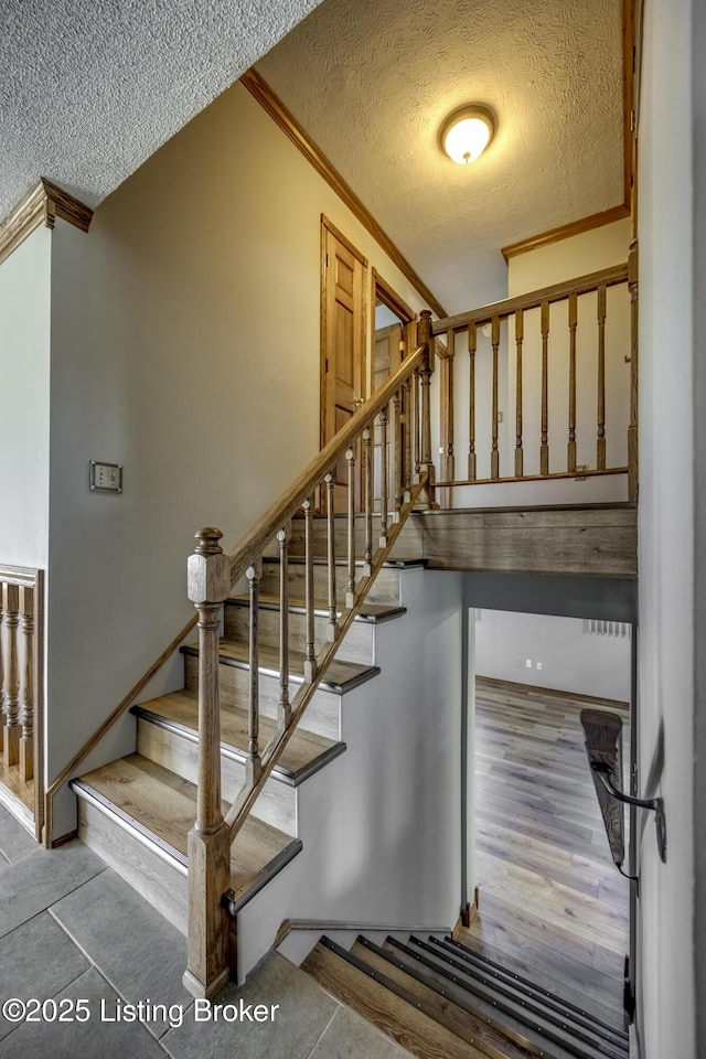 staircase with ornamental molding, a textured ceiling, and wood finished floors