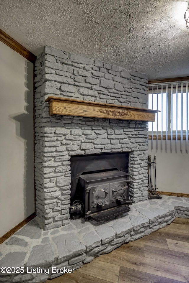 interior details with a textured ceiling, baseboards, wood finished floors, and a stone fireplace