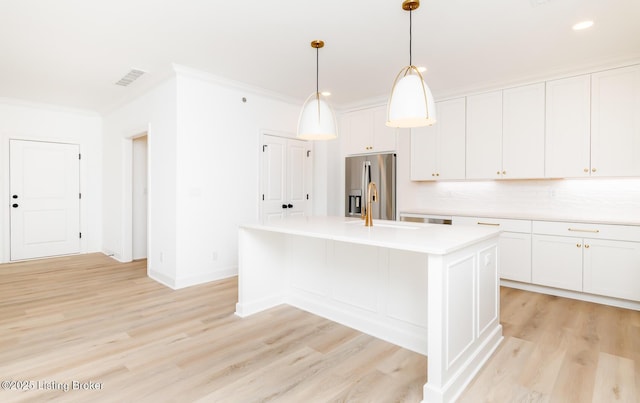 kitchen featuring crown molding, stainless steel refrigerator with ice dispenser, light countertops, visible vents, and an island with sink