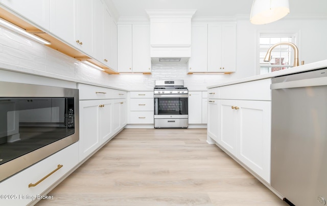 kitchen featuring stainless steel appliances, light countertops, backsplash, white cabinetry, and light wood-type flooring